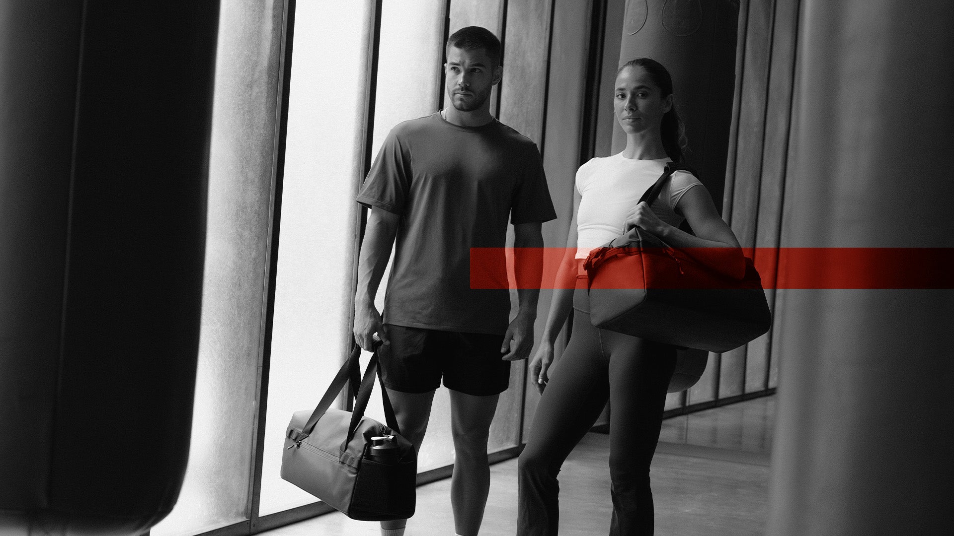 A man and woman standing on in a gym with gym dufffel 25l. The photo is in black and white with the Members Week creative over the top