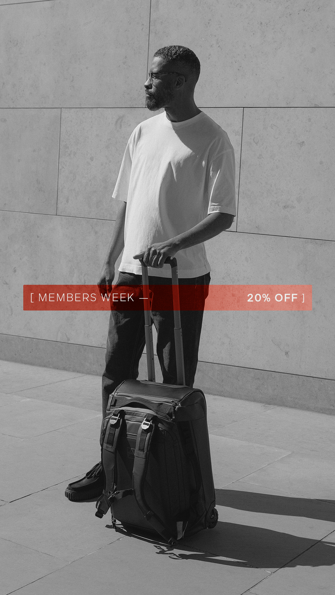 A man holding the extended handle of the Wheeled Duffel 40L in Black in Black and White with the creative of Members Week overlayed