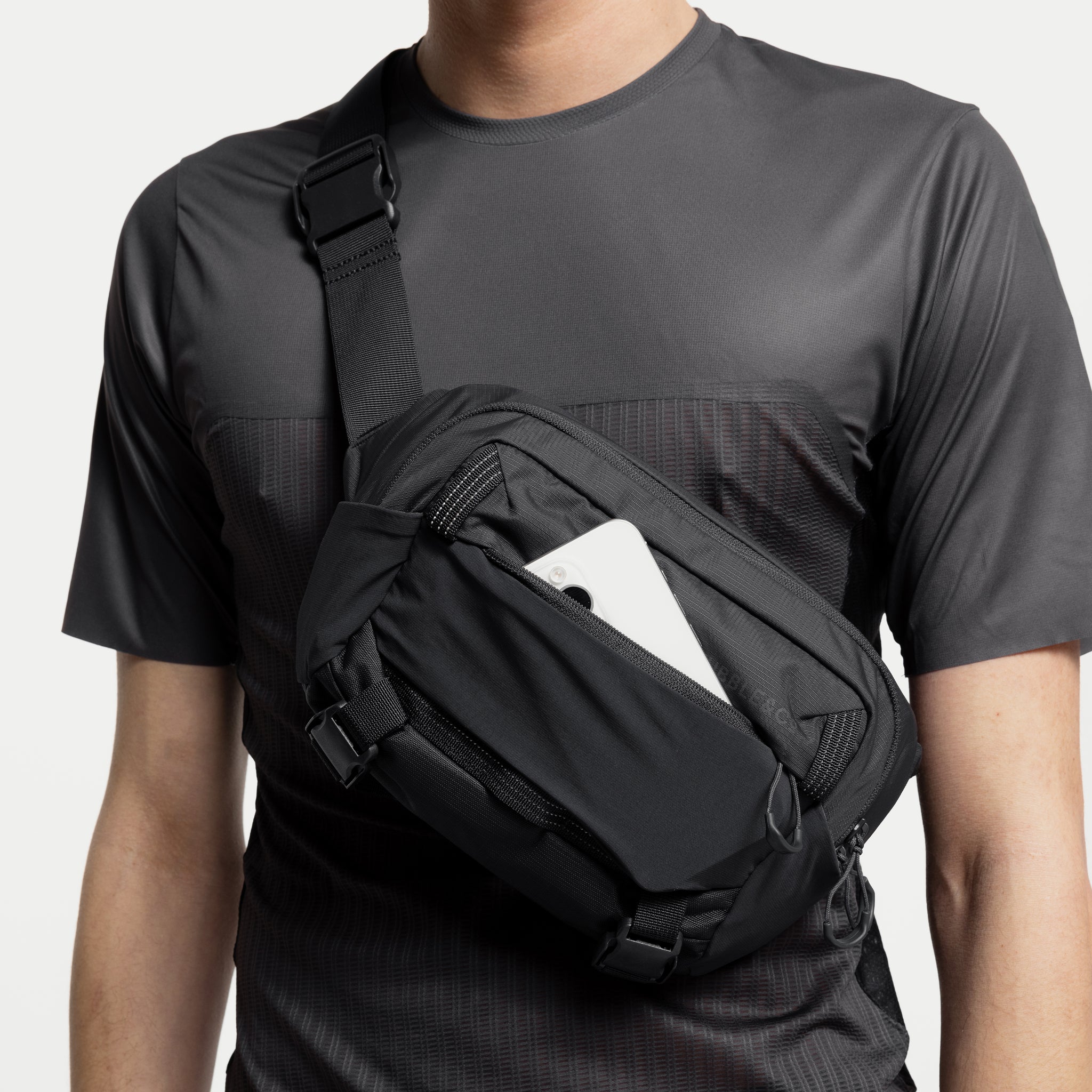 A studio shot of the front easy access pocket with a phone inside on the Ash, Charcoal and Magma Motion Sling 4L