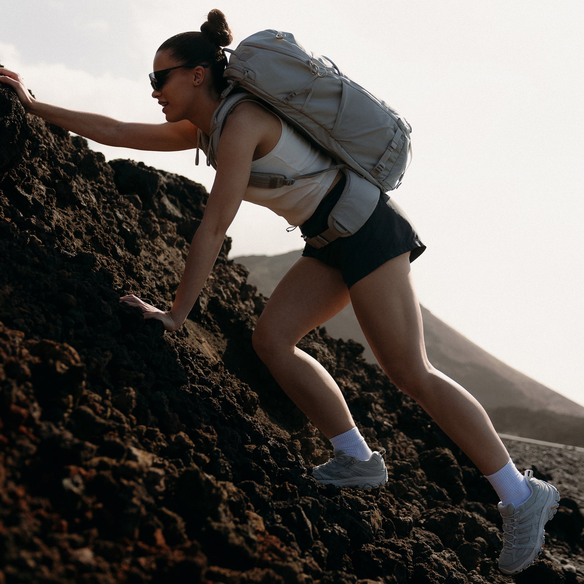 A woman hiking up a rock with a motion adventure pack 38l in Ash on her back
