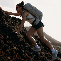 A woman hiking up a rock with a motion adventure pack 38l in Ash on her back