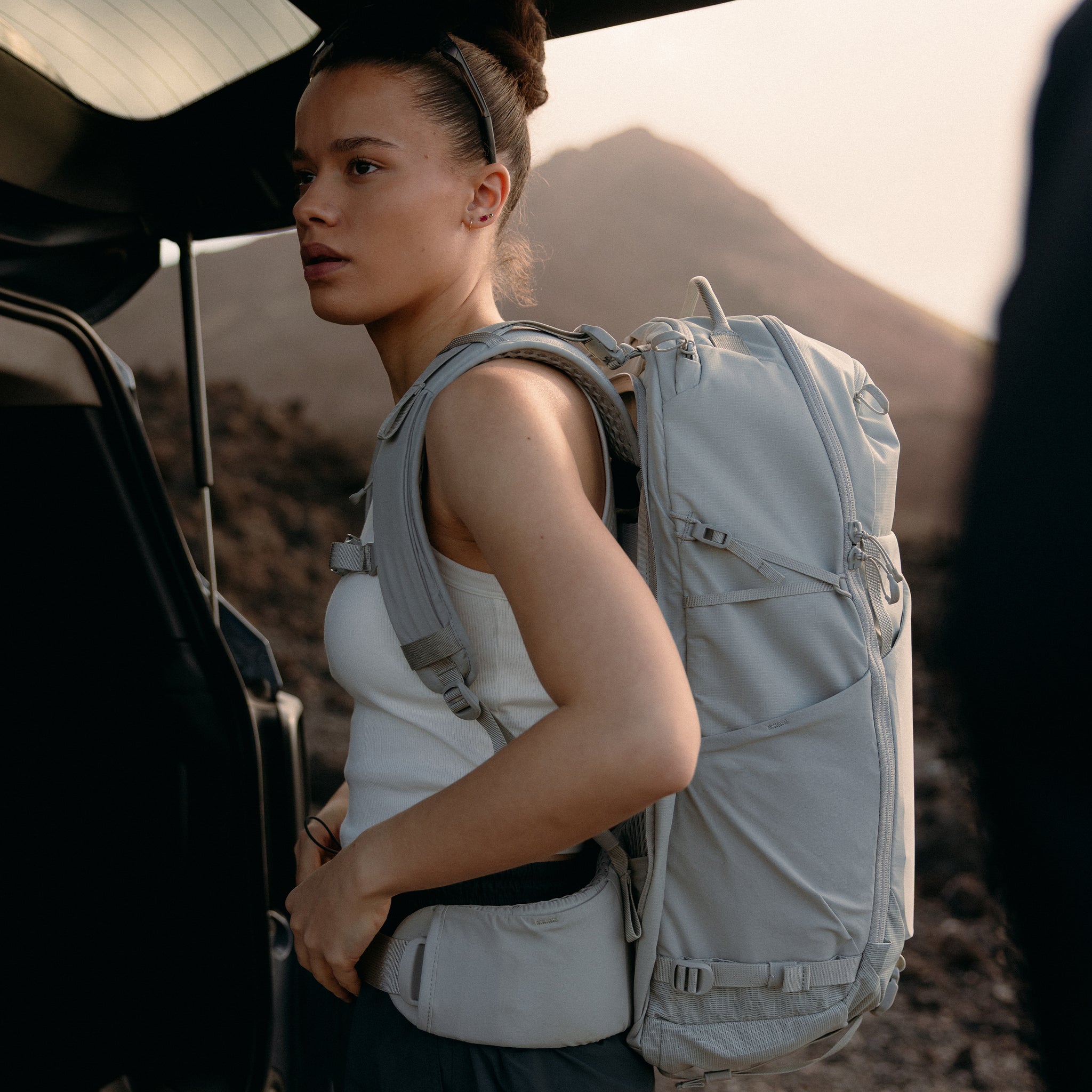 A woman adjusting the waist strap on her Motion Adventure Pack 38L on her back in Ash