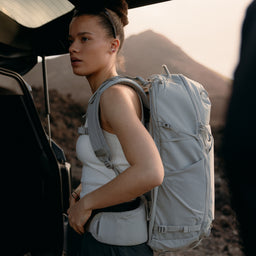 A woman adjusting the waist strap on her Motion Adventure Pack 38L on her back in Ash