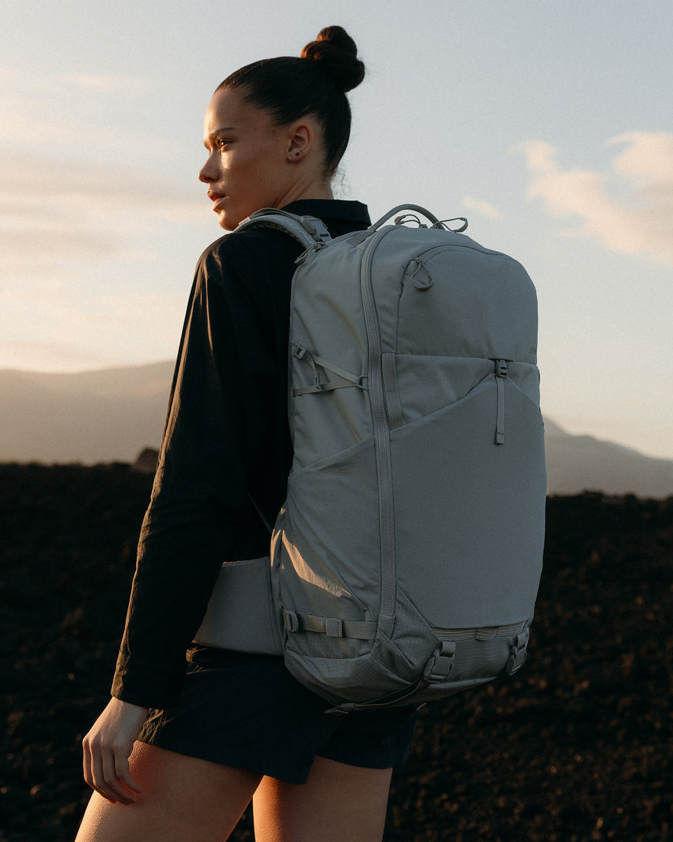 A woman looking into the sunset on a rocky landscape with a Motion Adventure Pack 8L on her back