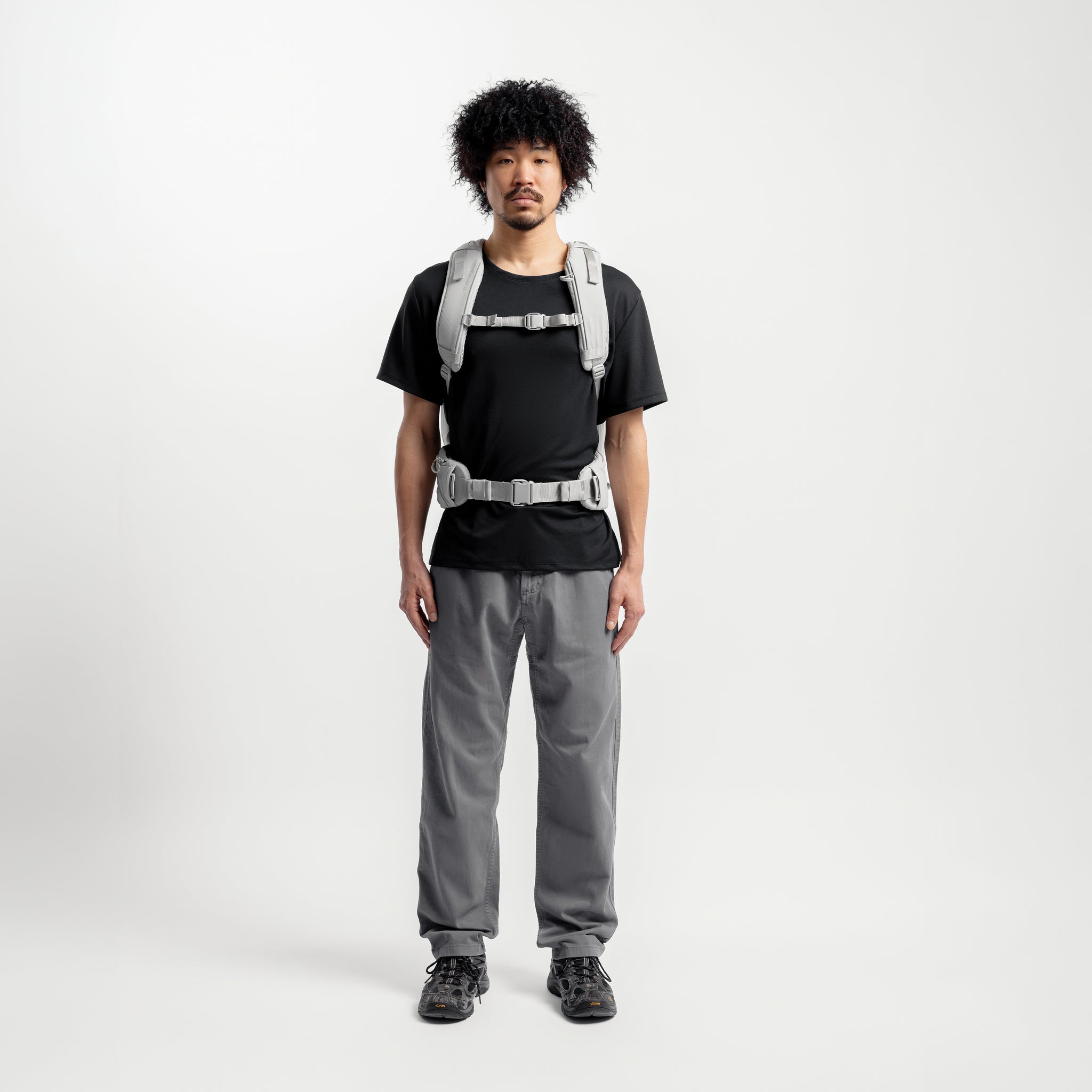 A studio shot of a model wearing the Motion Adventure Pack 38L in Ash with the chest and waist strap done up 