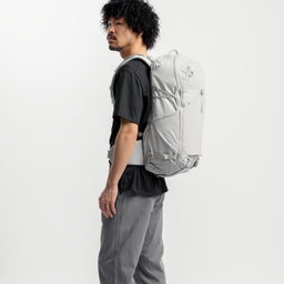 A studio shot of a model standing side on with the Motion Backpack 38L in Ash on his back 