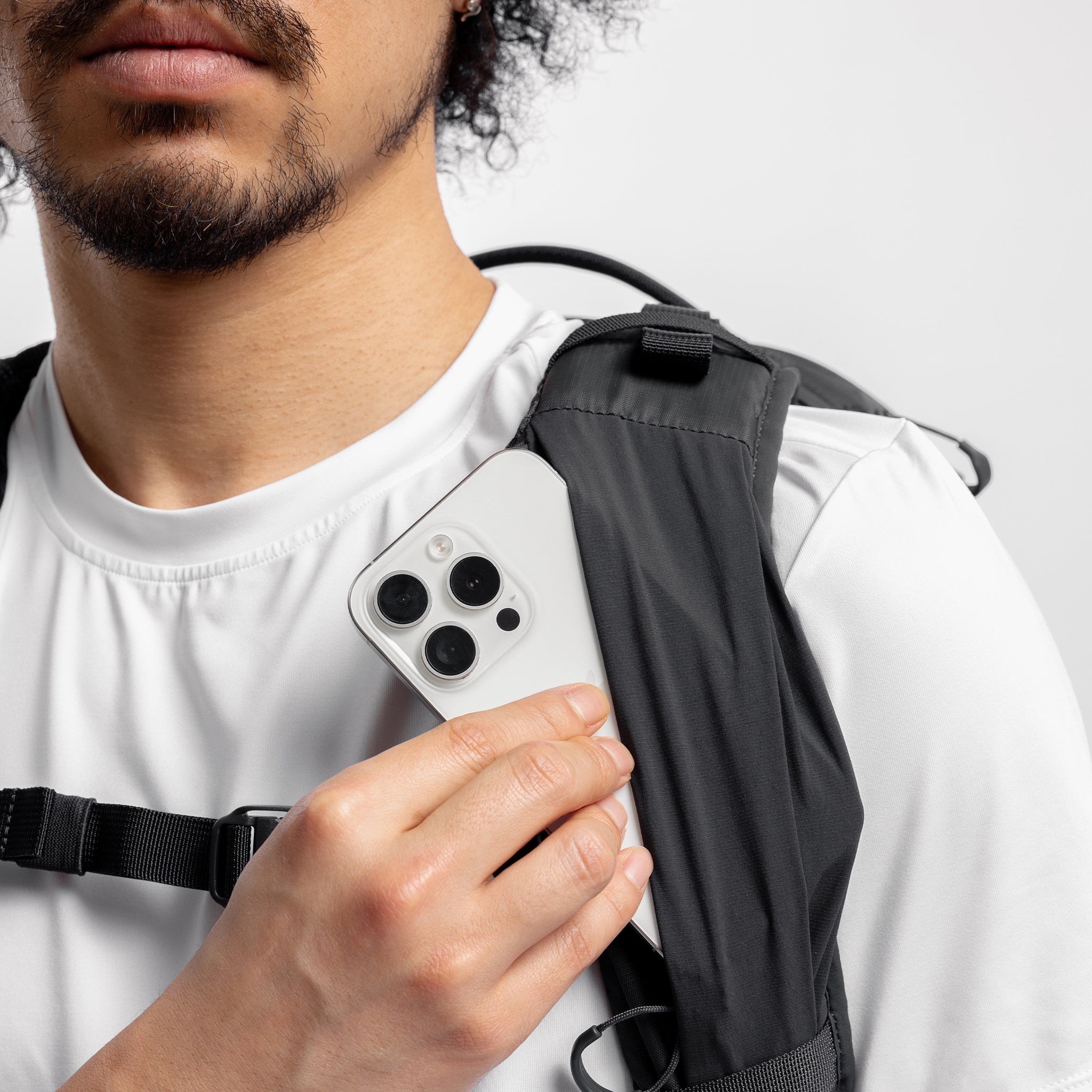 A model taking out the phone of the chest strap zip pocket on the Motion Adventure Pack 38L in Charcoal and Ash