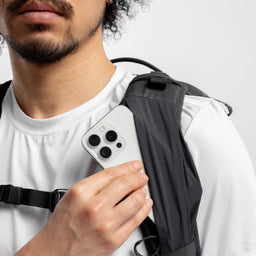 A model taking out the phone of the chest strap zip pocket on the Motion Adventure Pack 38L in Charcoal and Ash