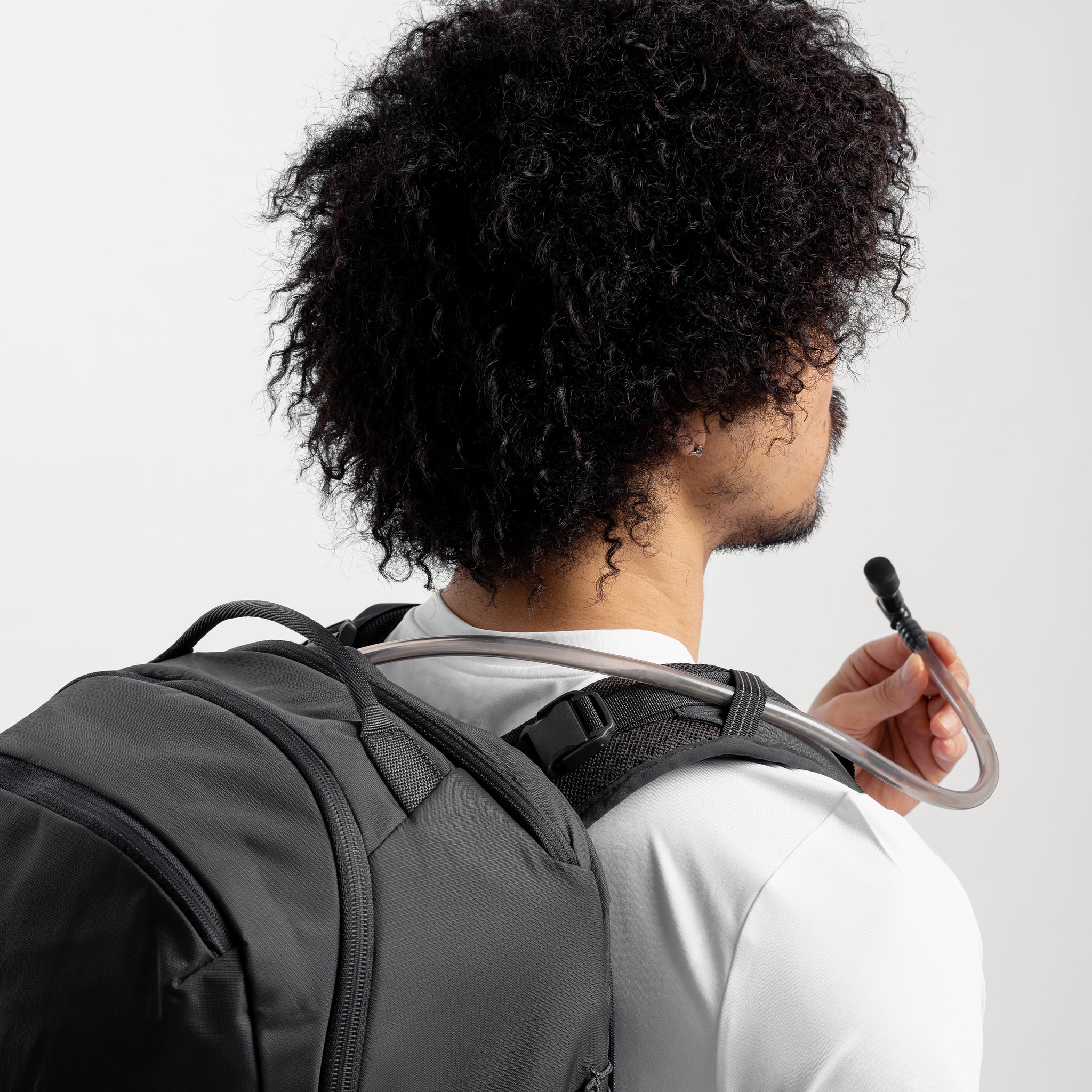 A man drinking from the hydration hose on the Motion Adventure Pack 38L in Charcoal