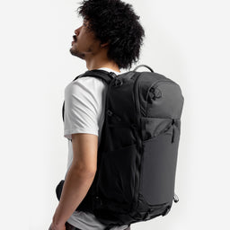 A studio shot of a model wearing the Motion Adventure Pack 38L in Charcoal on his back facing side on