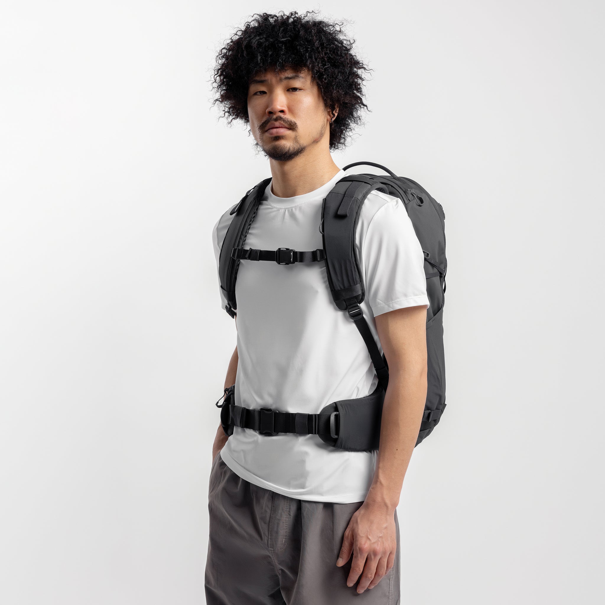 A studio shot of the model wearing the Motion Adventure Pack 38L in Charcoal on his back with the waist straps and chest straps done up
