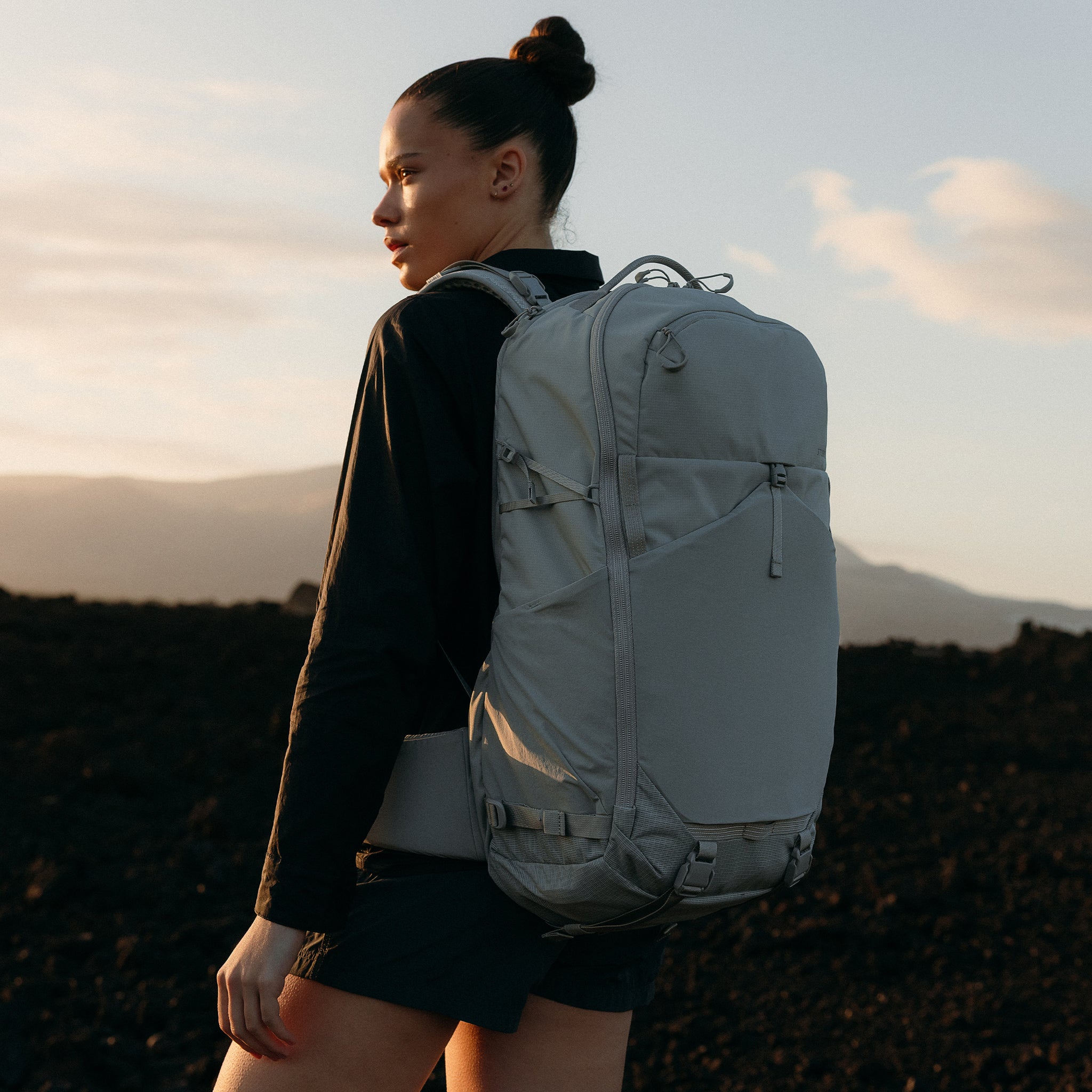A woman standing in the sunset with a Motion Adventure Pack 38L on her back in Ash