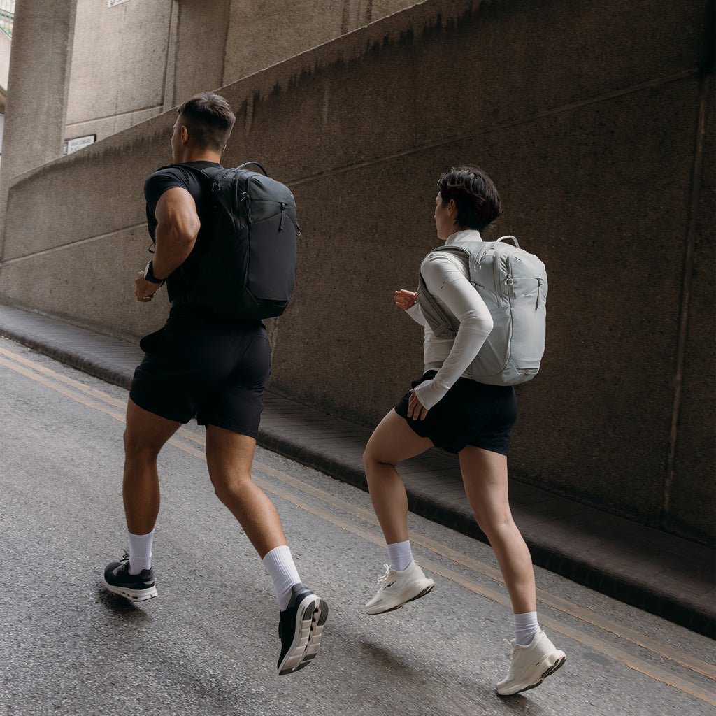 A man and woman running up a hill on the road wearing a motion backpack 20l in charcoal and ash