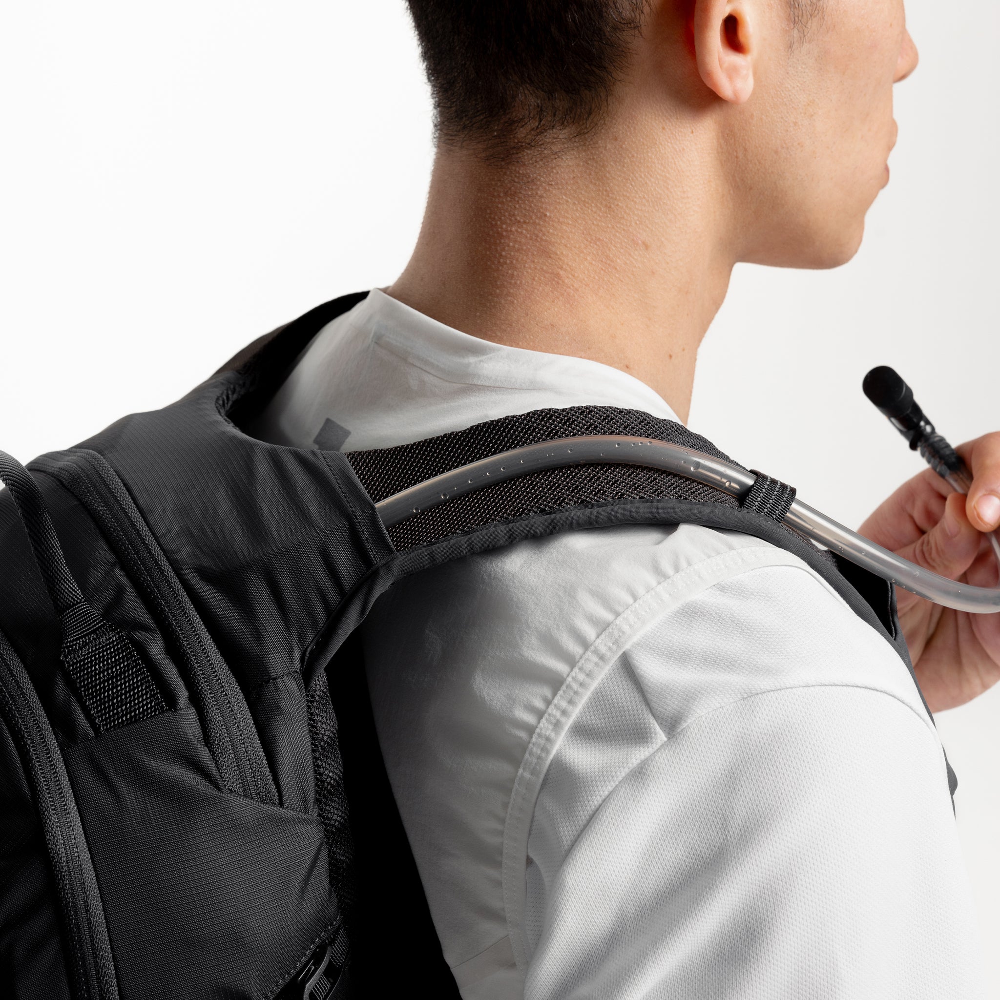 A studio shot of a model taking a drink from the hydration reservoir within the Charcoal Motion Backpack 20L as well as Magma and Ash Backpack 20Ls