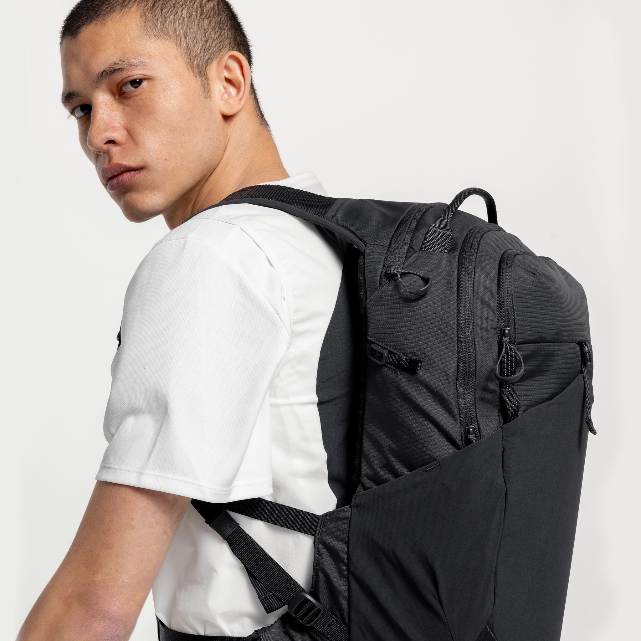 A studio shot of a man standing side on wearing a Charcoal Motion Backpack 20L on his back