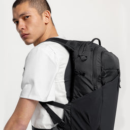 A studio shot of a man standing side on wearing a Charcoal Motion Backpack 20L on his back