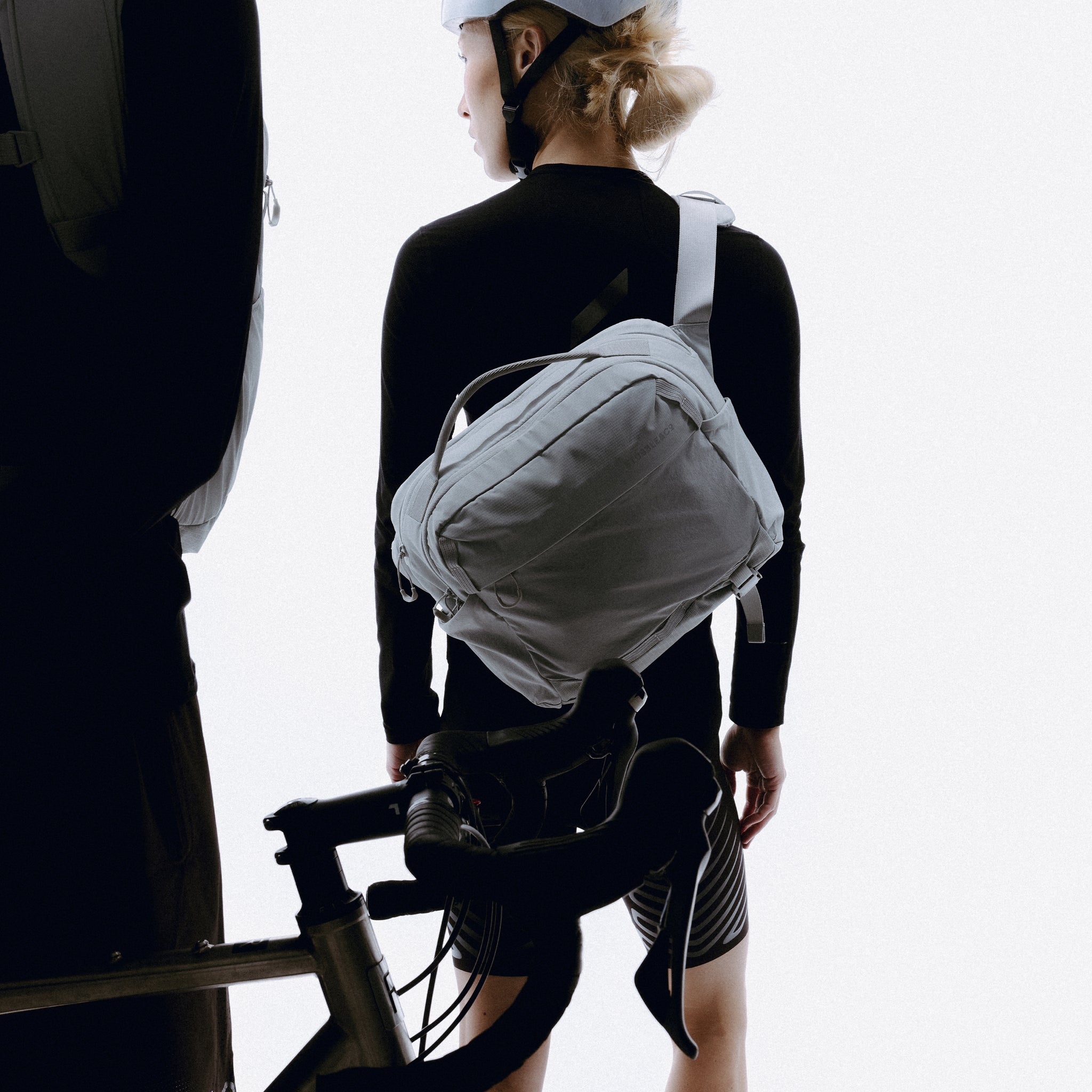 A woman wearing a motion sling 15l in Ash on her back next to her bike