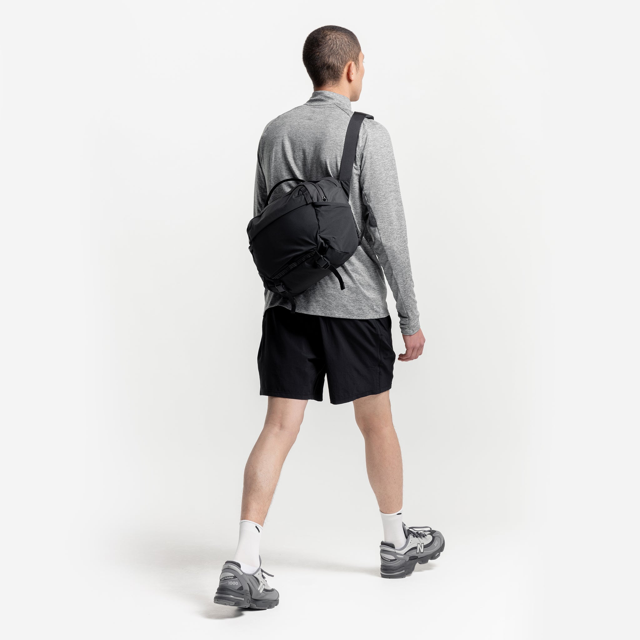A studio shot of a man walking wearing a Charcoal Motion Sling 15L on his back