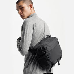 A studio shot of a man wearing the Charcoal Motion Sling 15L on his back