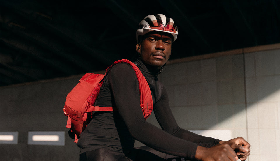 A man looking into the camera sitting on a bike wearing a helmet and magma sling 15l on his back using the crossbody strap