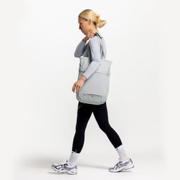 A studio shot of a woman walking with an Ash Motion Tote Pack 18L on her shoulder