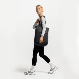 A studio shot of a woman walking with a Charcoal Motion Tote Pack 18L on her shoulder