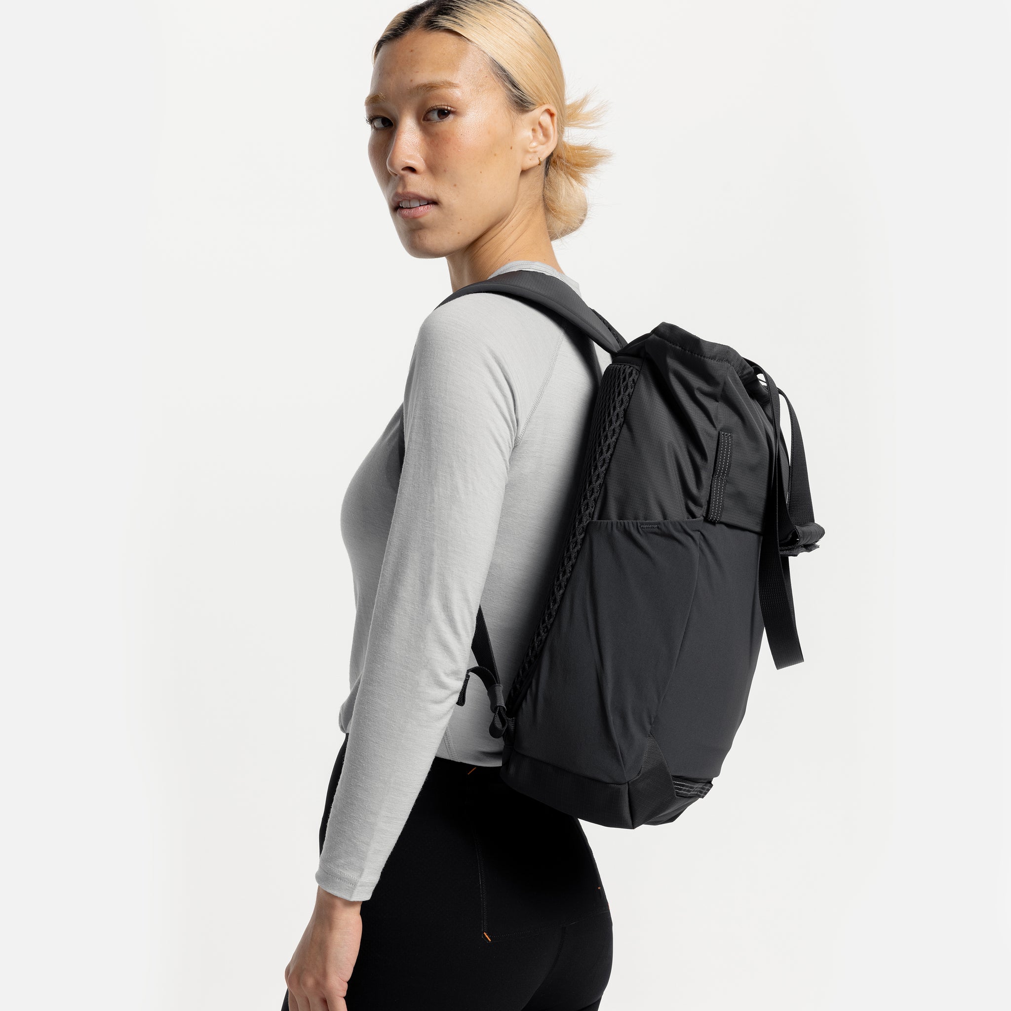 A studio shot of a model standing side on wearing a Charcoal Motion Tote Pack 18L on her back