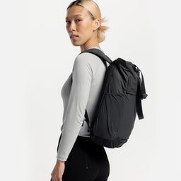 A studio shot of a model standing side on wearing a Charcoal Motion Tote Pack 18L on her back