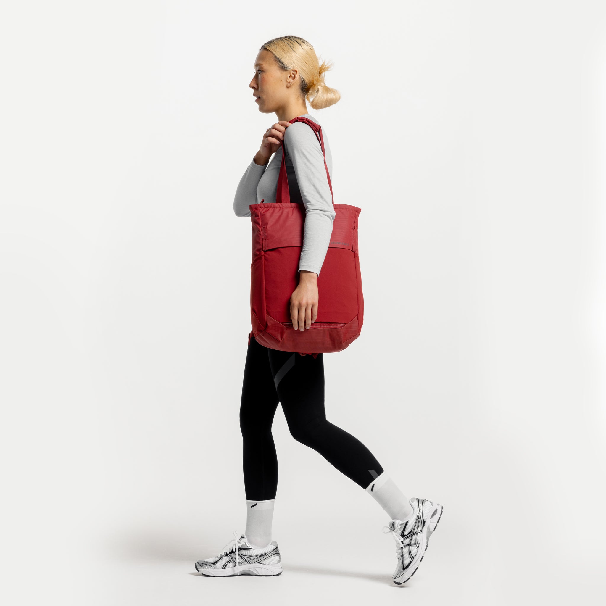 A studio shot of a woman walking with a Magma Motion Tote Pack 18L on her shoulder