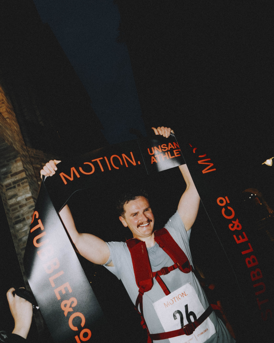 A man holding up the finish line banner at the Stubble & Co x Sanctioned Athletics event wearing a magma backpack 20l on his back