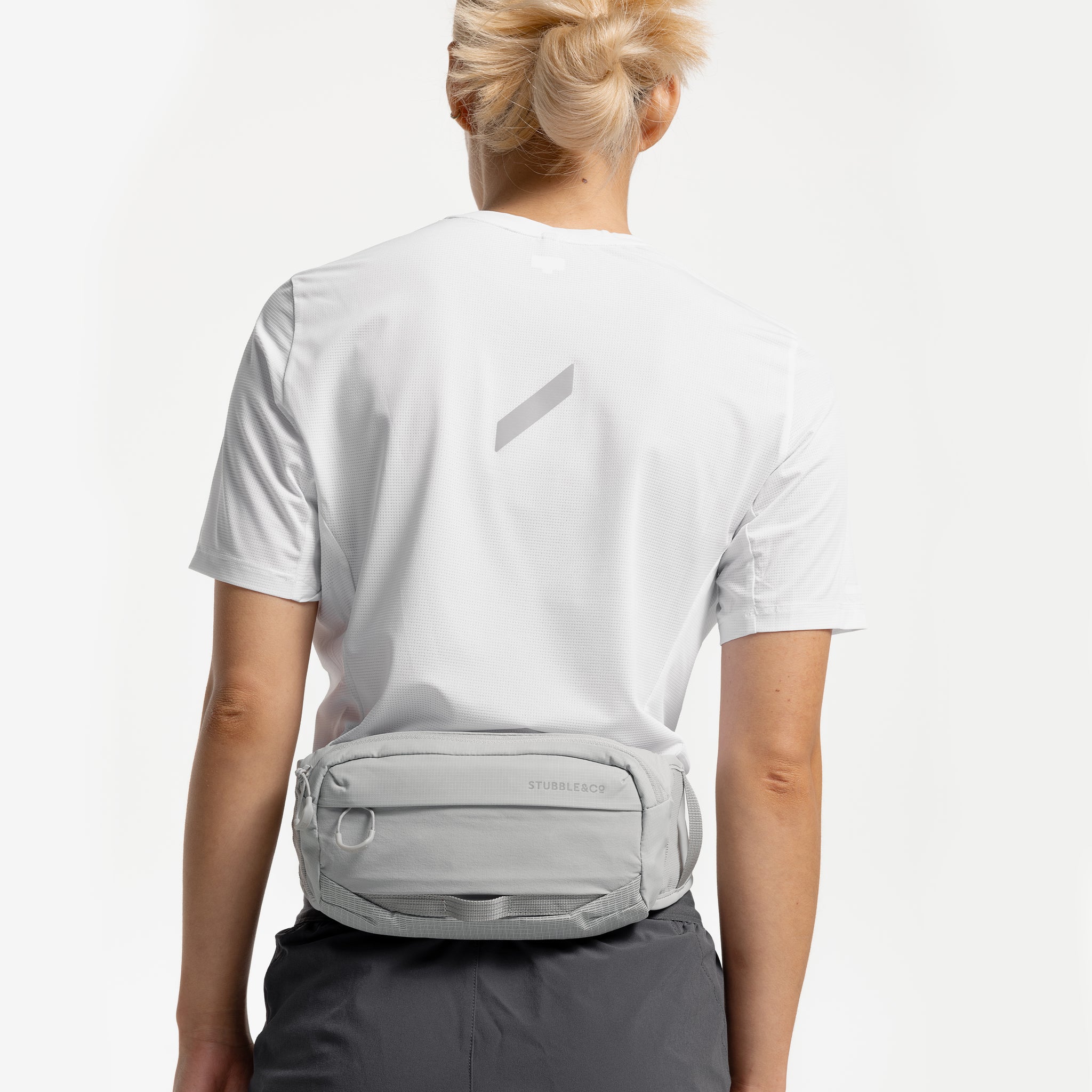 A studio shot of a woman wearing an Ash Motion Waist Pack 2L around her waist on her back