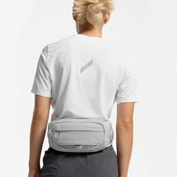 A studio shot of a woman wearing an Ash Motion Waist Pack 2L around her waist on her back