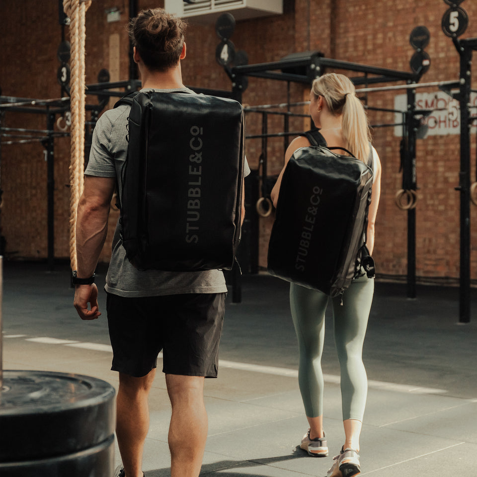 Man and women wearing The Kit Bag All Black Backpack at the gym