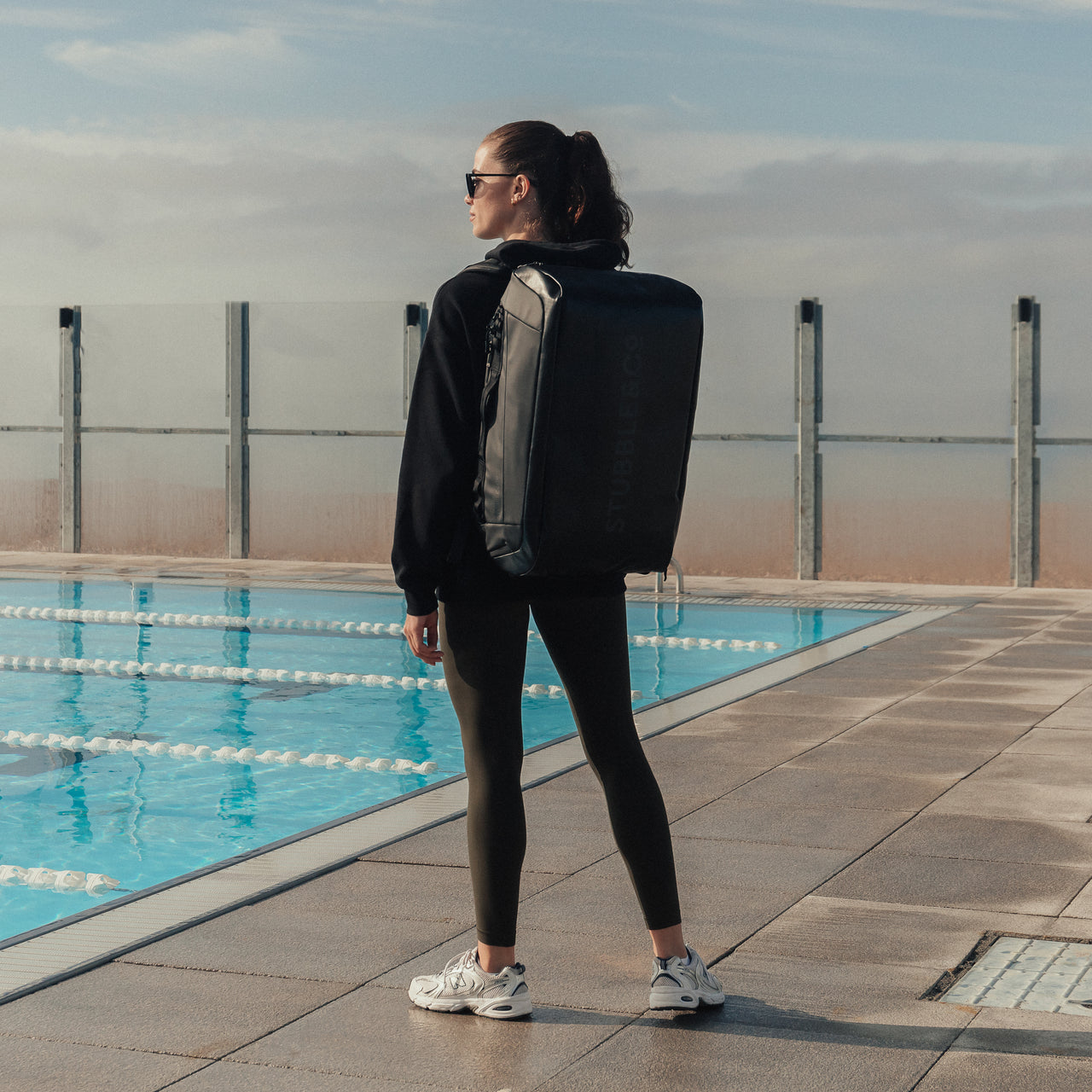 Women wearing The Kit Bag All Black Backpack by swimming pool