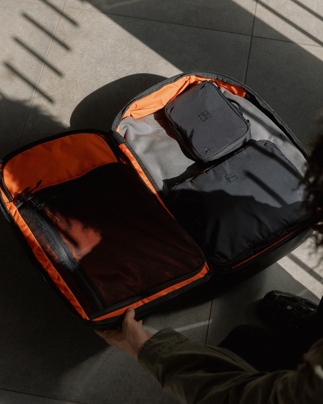 Travel backpack open, showing the orange interior with All Black packing cubes and clothes inside.