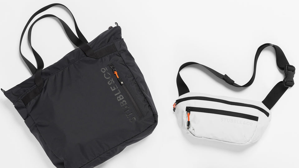A studio flat lay of a black packable tote and white packable sling