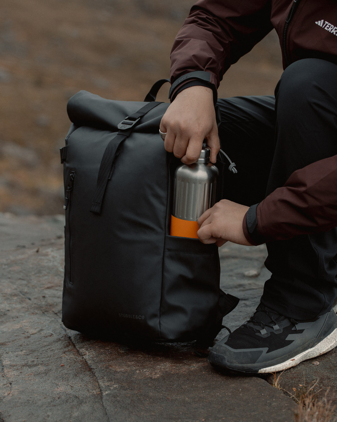 Person taking a water bottle from the side pocket of a roll top backpack.