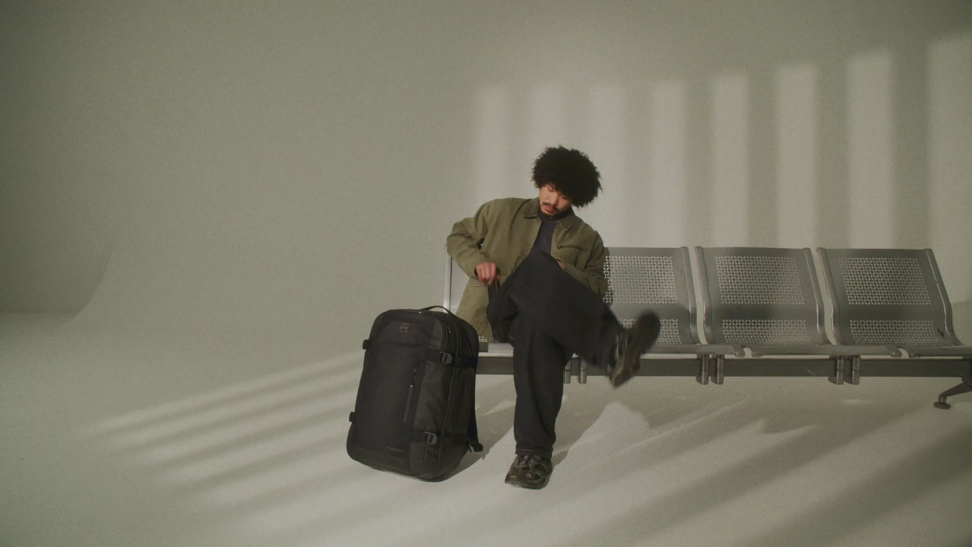 A video of a man sitting on an airport bench with a travel backpack 40l- 16:9