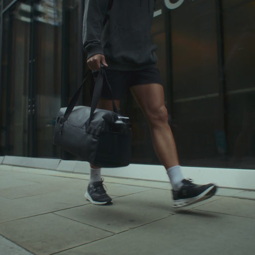 A campaign video for the gym duffel 25L in All Black showing a man going to the gym and a woman going on a run and doing yoga