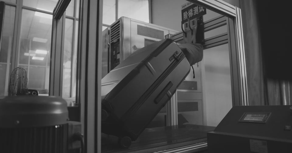black hardshell suitcase being testing in a factory for durability.