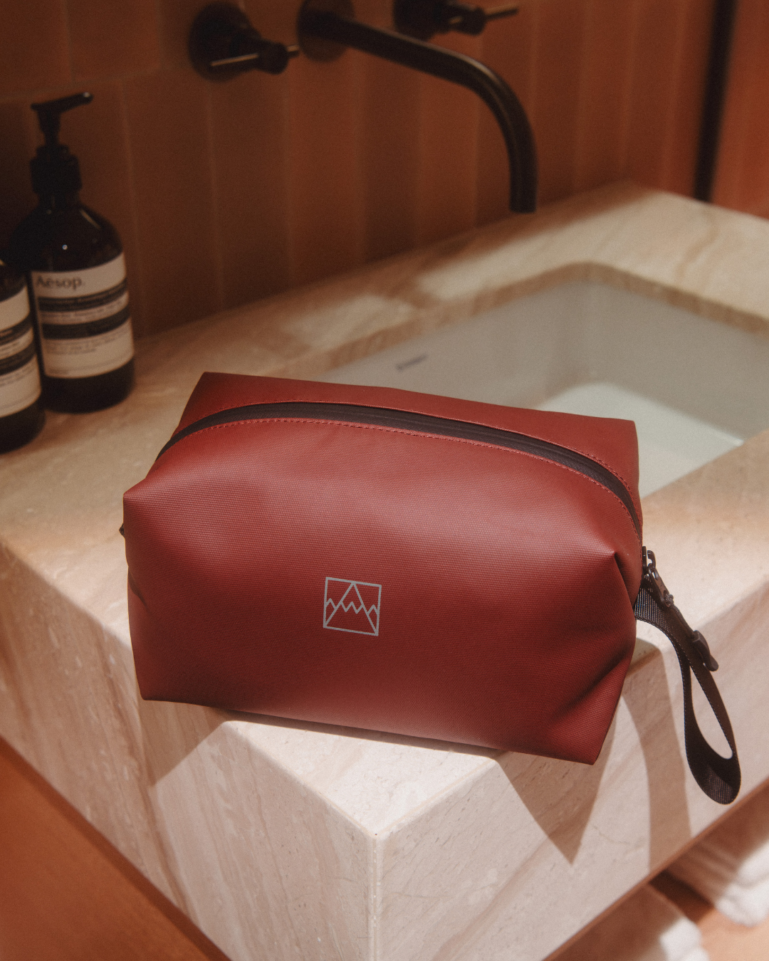 Garnet Red Wash Bag sitting on the edge of a hotel sink.