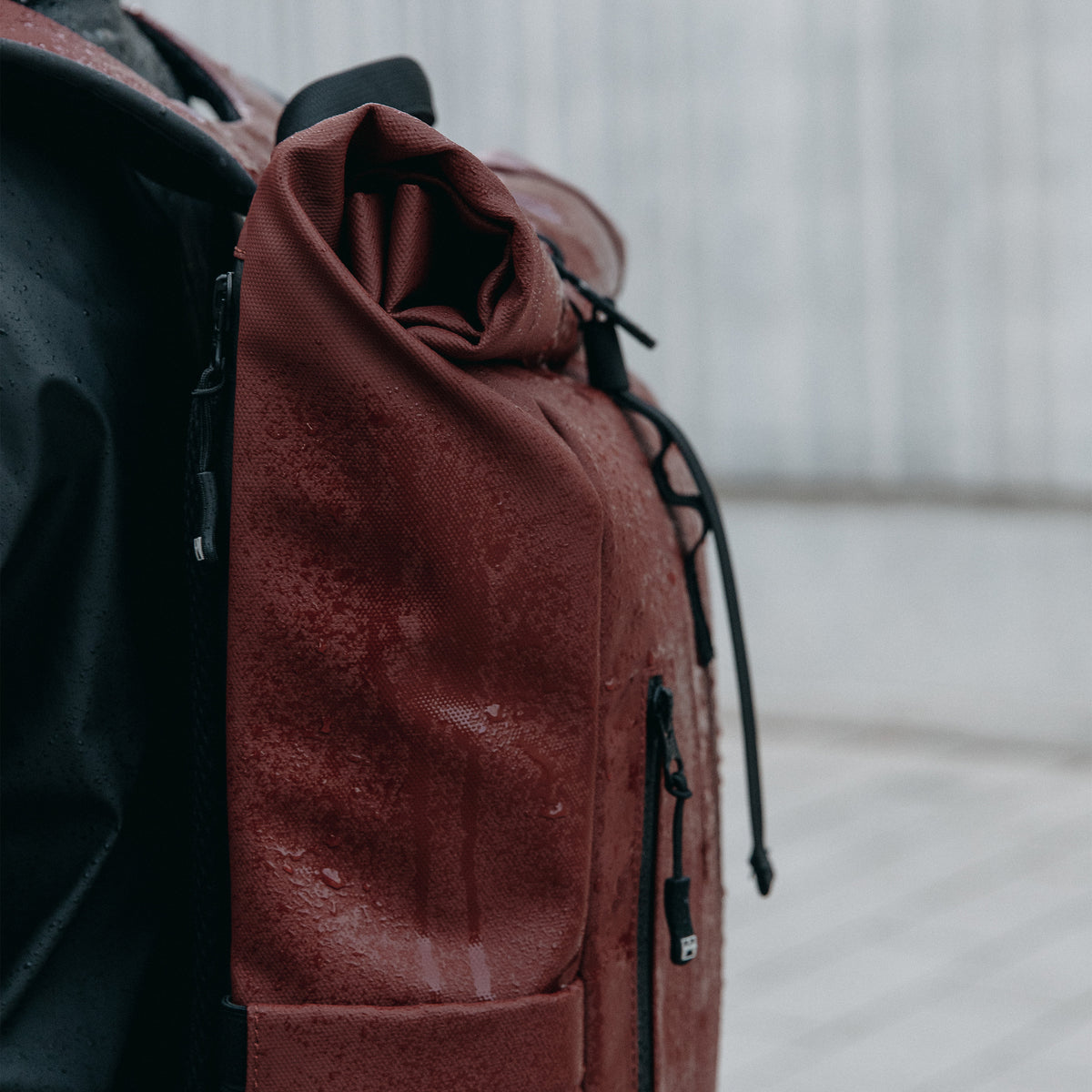 A close up of the rain on the waterproof material on the roll top 15l in garnet red on a woman's back