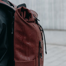 A close up of the rain on the waterproof material on the roll top 15l in garnet red on a woman's back