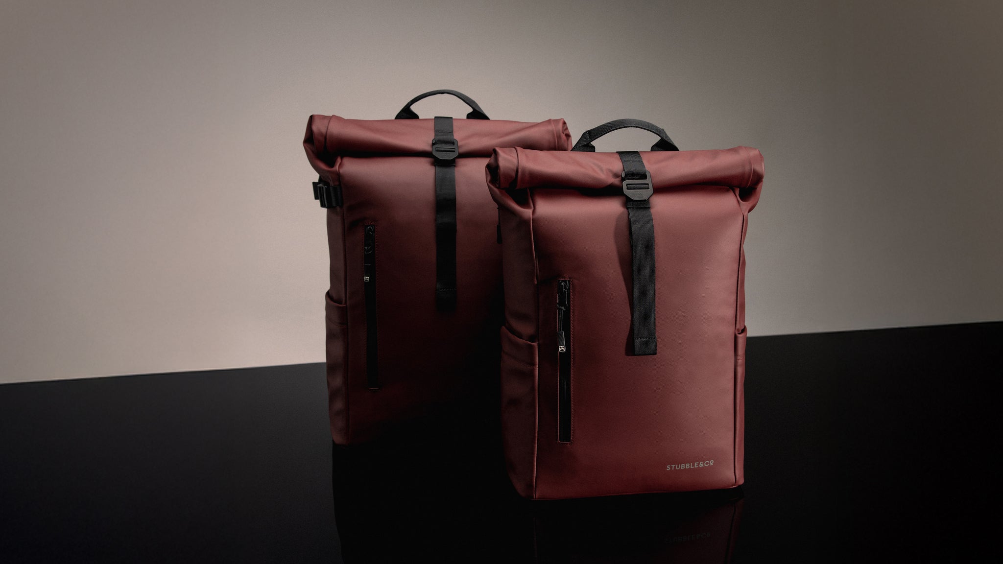 Two red roll-top bags with black straps on a dark surface and gray background