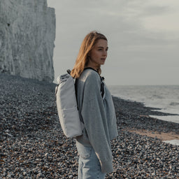 Women wearing The Roll Top 15L in Arctic White on a pebble beach