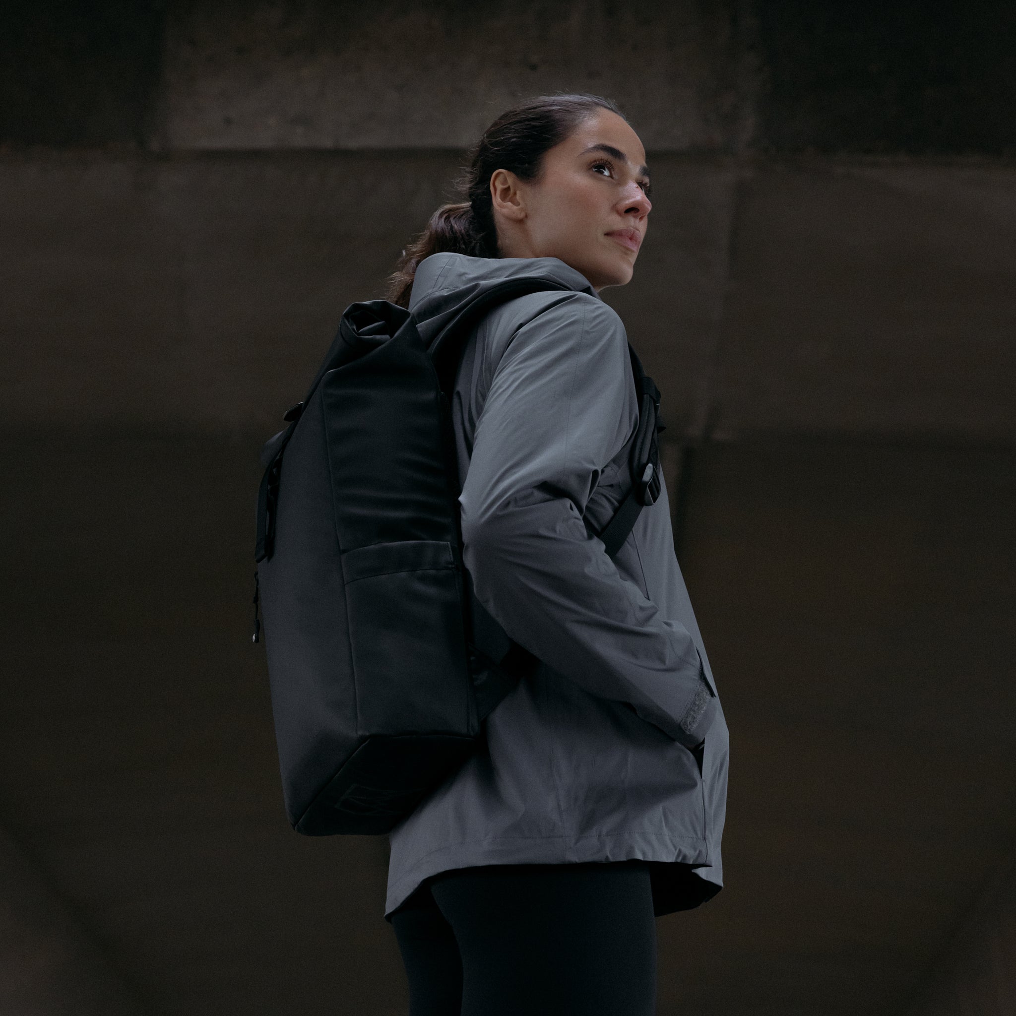 A woman wearing an  All Black Roll Top 15L backpack on her backpack