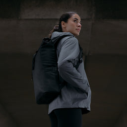 A woman wearing an  All Black Roll Top 15L backpack on her backpack