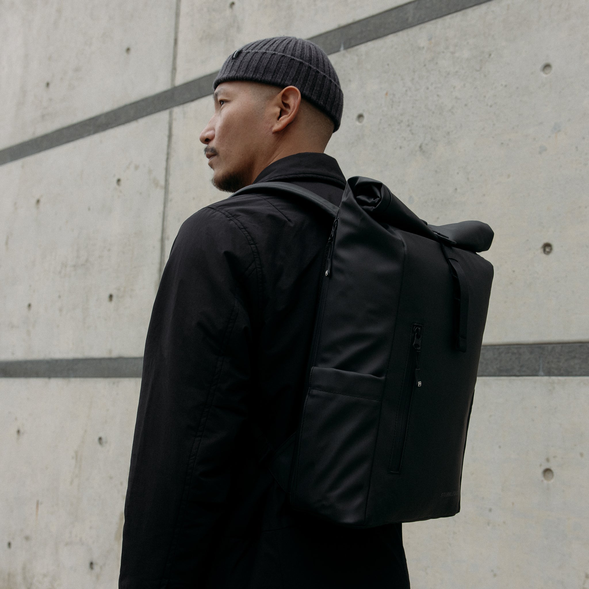 A man wearing a Roll Top 15L backpack on his back in All Black
