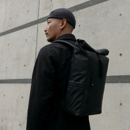 A man wearing a Roll Top 15L backpack on his back in All Black