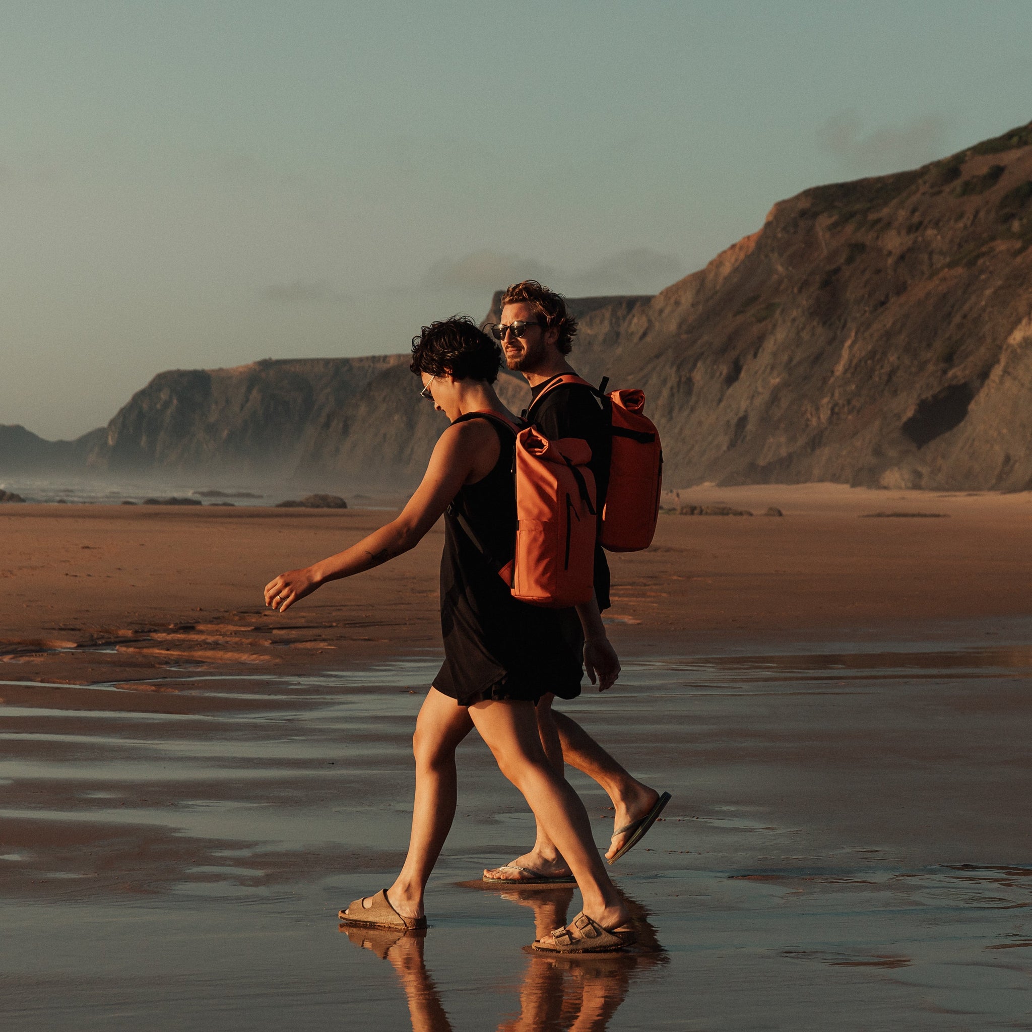 Man and women wearing The Roll Top 15L in Ember Orange on a beach